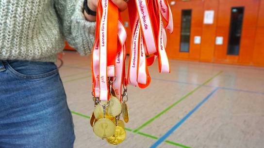 Eine Person hält die Medaillen für die Teilnehmenden des Fussballturniers in die Kamera.