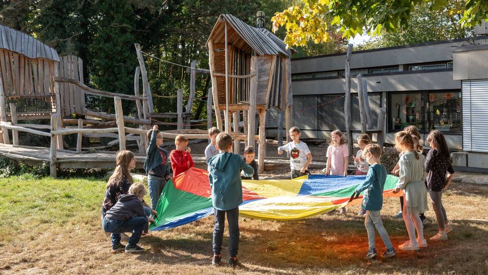 Grndschulschüler:innen und Lehrkräfte schwingen gemeinsam ein buntes Schwingtuch.