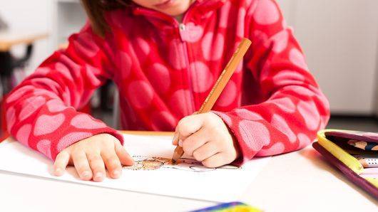 Kind sitzt am Tisch und schreibt auf einem Blatt Papier.