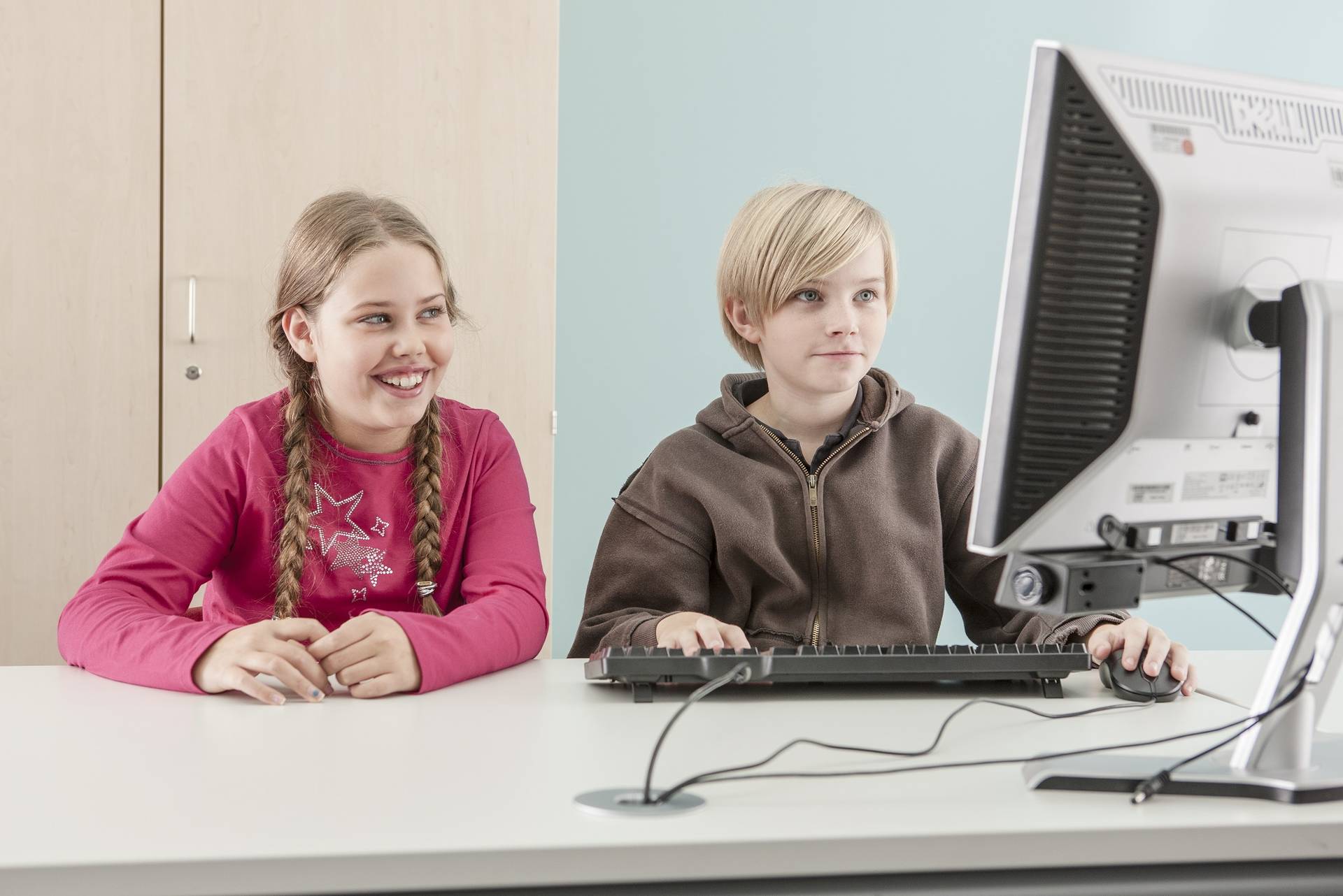 Eine Schülerin mit geflochtenen Zäpfen und ein Schüler gucken interessiert auf einen Bildschirm.