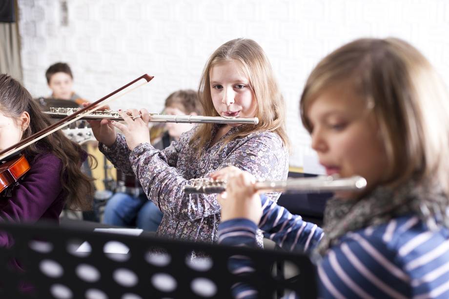 Schülerorchester macht Musik. Im Vordergrund spielen zwei Schülerinnen Querflöte.