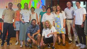 Auf der Bühne wird der Kooperationspreis an das Organisationsteam des Bandworkshops verliehen. Zwölf Personen stehen auf der Bühne und schauen freundlich in die Kamera.