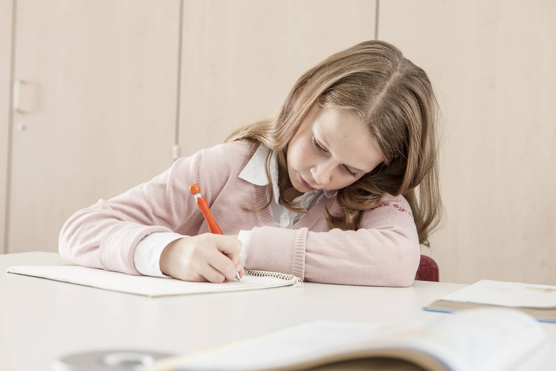 Schülerin schreibt mit einem Kugelschreiber ihre Gedanken in einen Collegeblock.
