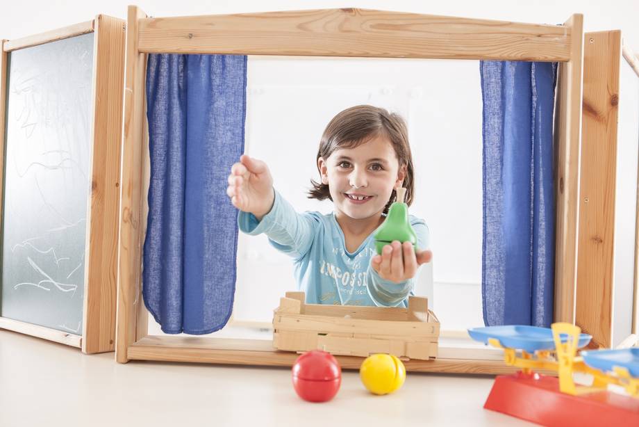 Schülerin schaut durch einen Holzverkaufsladen und bietet Spielobst aus Holz an.