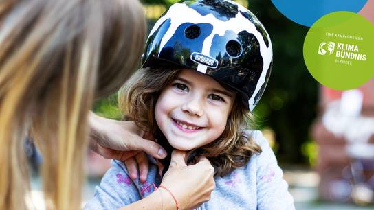 Frau hilft Mädchen beim Befestigen des Fahrradhelmes; Werbebild für STADTRADELN 2026