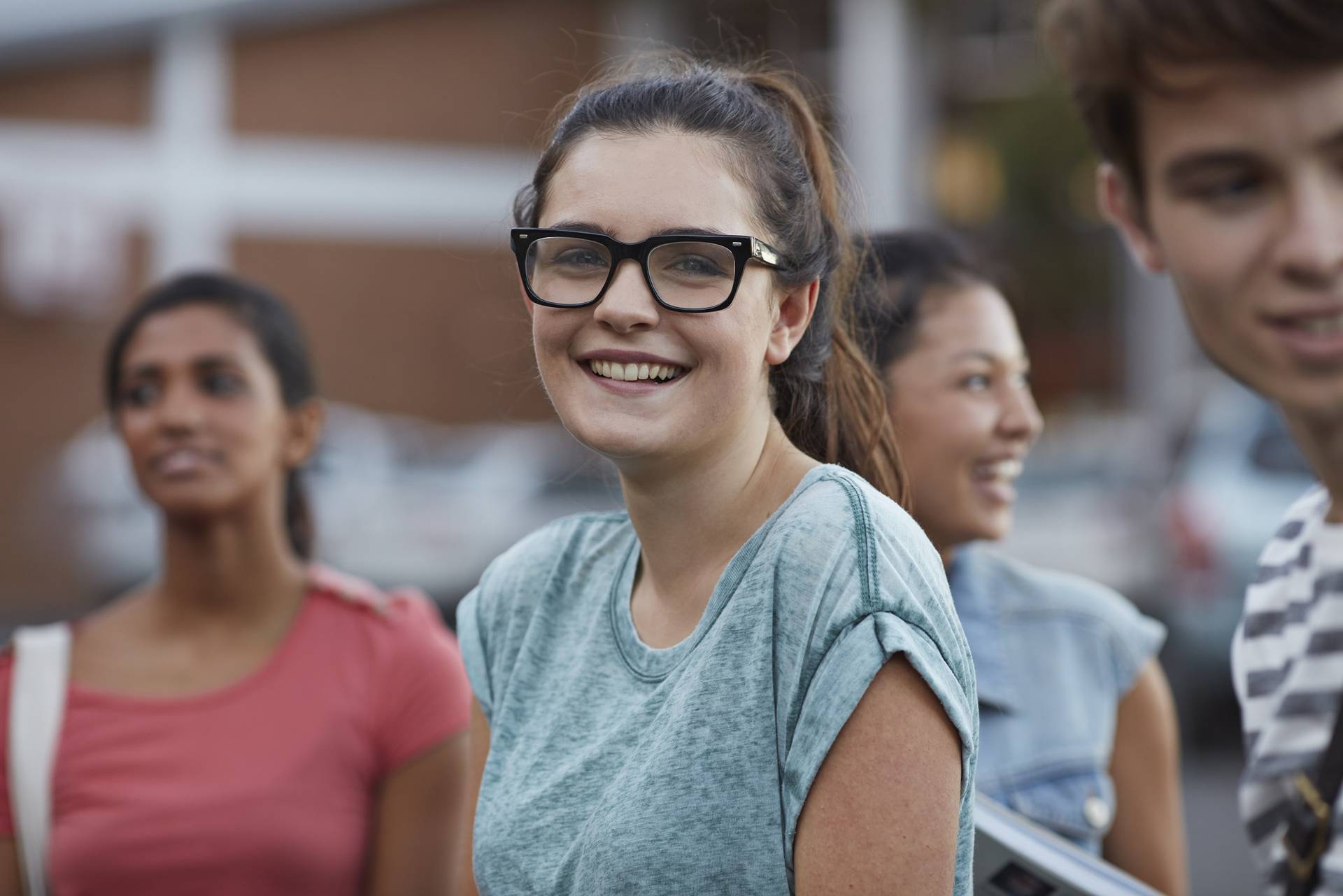 Gruppe junger Menschen mit einer lachenden Frau mit markanter Brille im Vordergrund.