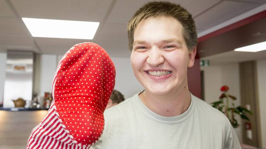 Schüler hält eine Handpuppe in der Hand und lacht in die Kamera.