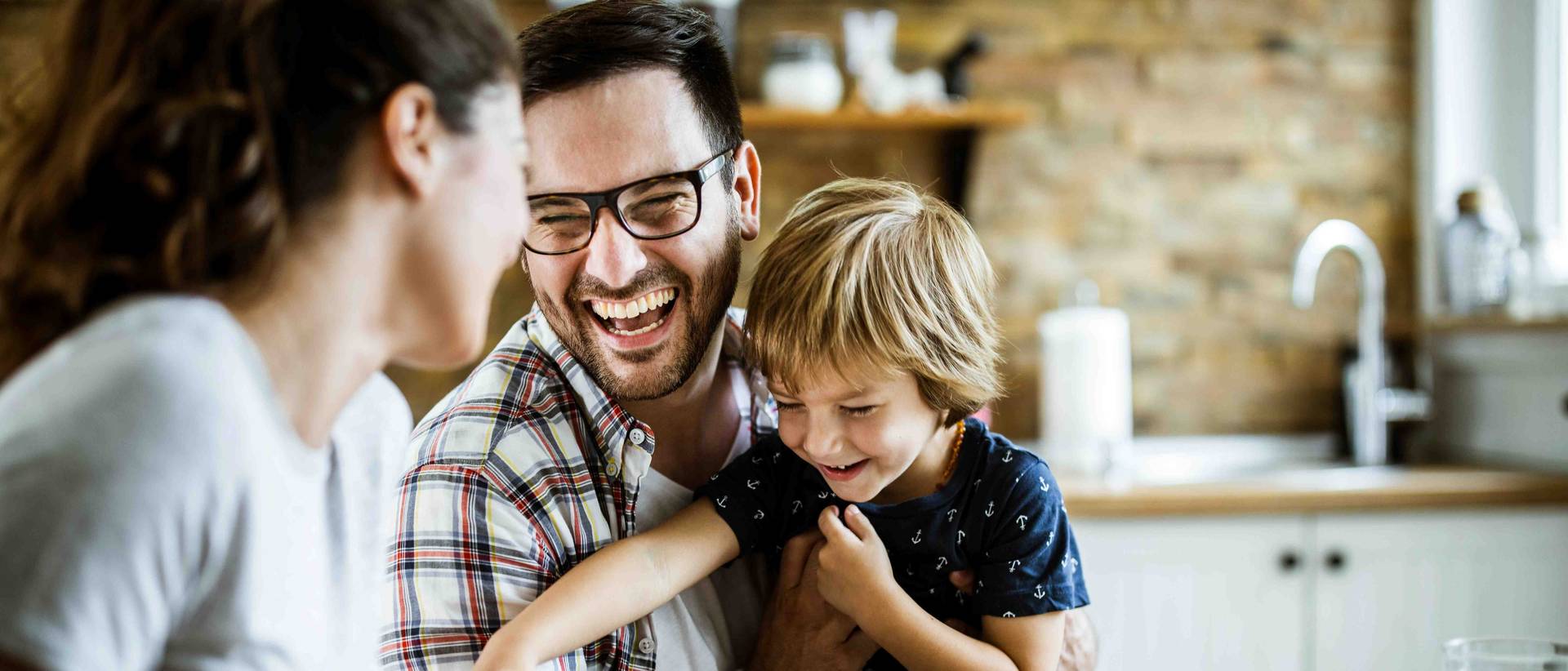 Kleine Familie, bestehend aus Mutter, Vater und Kind, sitzen am Esstisch und lachen gemeinsam.