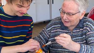 Schüler bemalt gemeinsam mit einer Seniorin mithilfe eines Pinsels ein Osterei.
